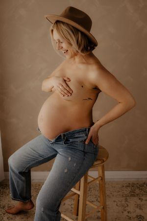 Casual maternity photos with denim jeans and natural posing on wooden stool.