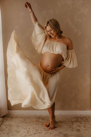 Elegant maternity portrait series featuring a flowing white off-shoulder dress against a neutral backdrop.