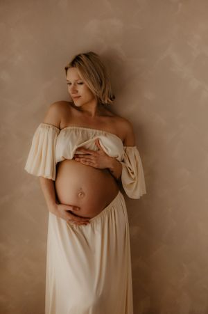 Intimate maternity portraits featuring gentle poses and delicate white off-shoulder dress.