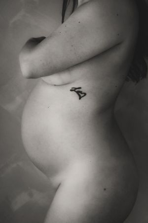 An intimate black and white maternity photo showing a small tattoo on the side of a pregnant belly.