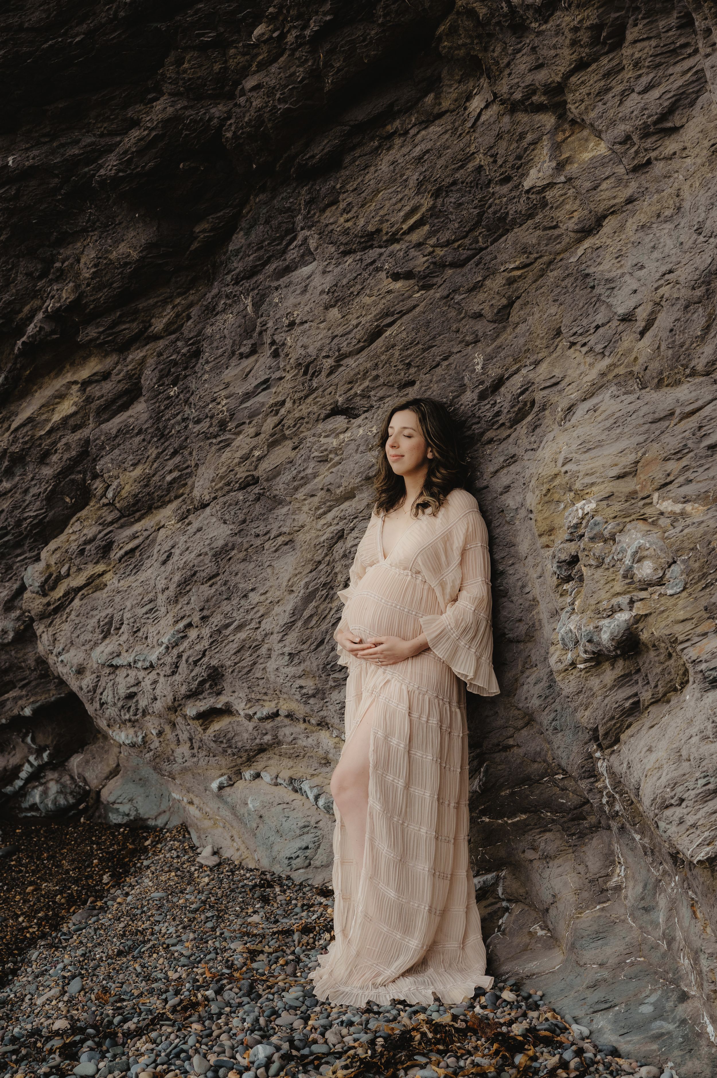 Maternity portrait against textured rock wall with woman in flowing beige dress.