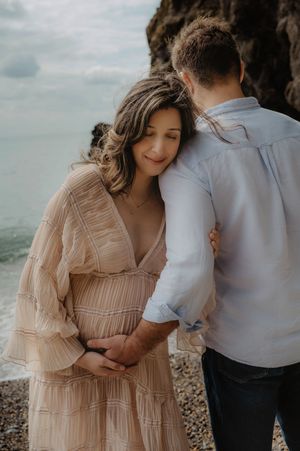 Intimate maternity portrait of couple embracing on rocky beach at sunset.
