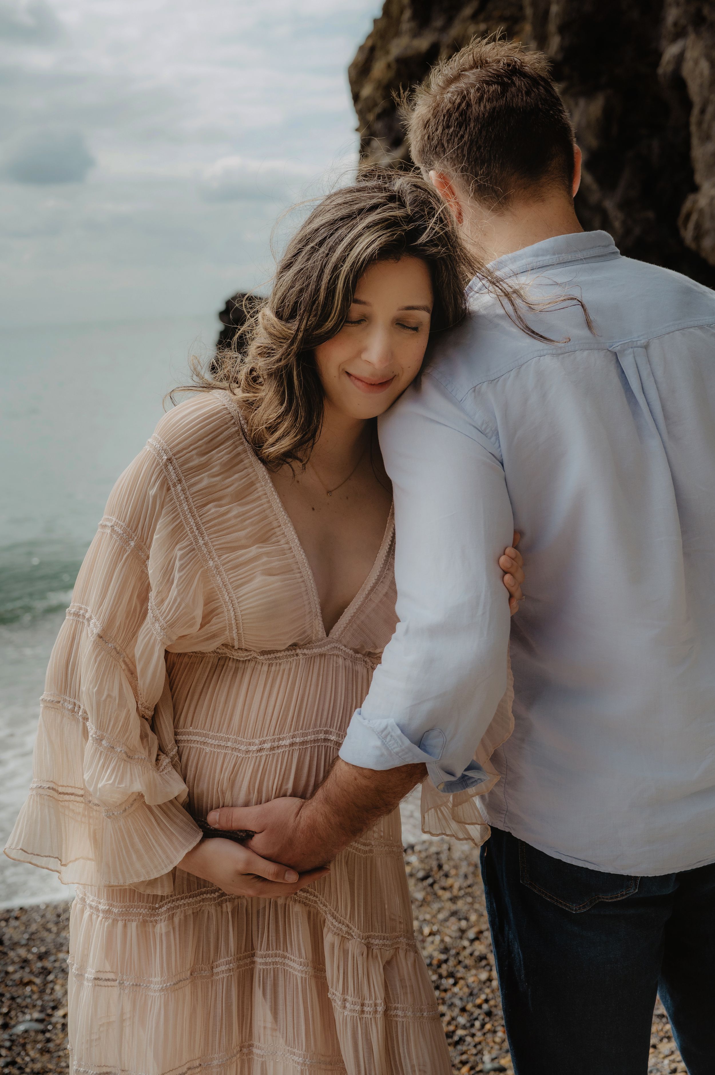 Intimate maternity portrait of couple embracing on rocky beach at sunset.