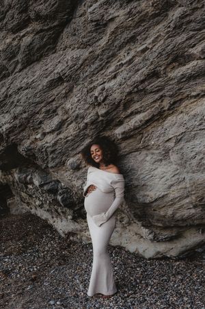 A maternity portrait session against dramatic rocky cliffs in a fitted white dress.