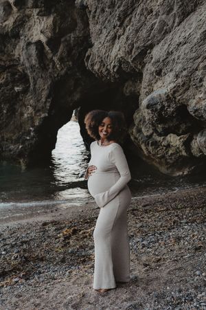 A maternity photo captured in a sea cave wearing a form-fitting white dress.