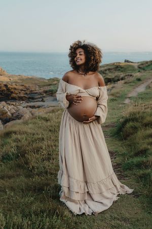 A beige dress flows in the wind during a seaside maternity photo session.