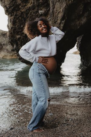 A casual maternity photo in jeans and sweater near ocean caves.