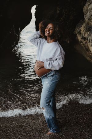 A casual maternity moment captured in denim and sweater by the ocean caves.