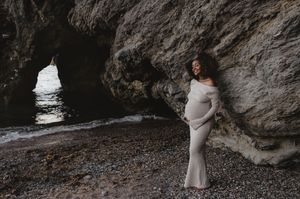 A coastal maternity portrait with a natural rock arch and ocean backdrop.