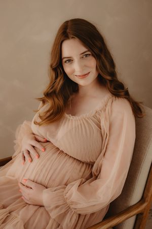 Soft maternity portraits in blush tones featuring a flowing long-sleeved dress.