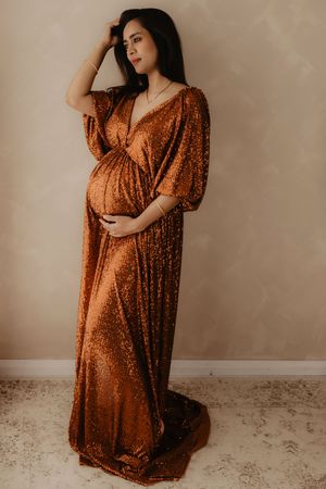 Glamorous maternity photo of an expectant mother in a sparkly copper evening gown.