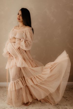 An expectant mother in a flowing blush gown twirls during her maternity photoshoot.