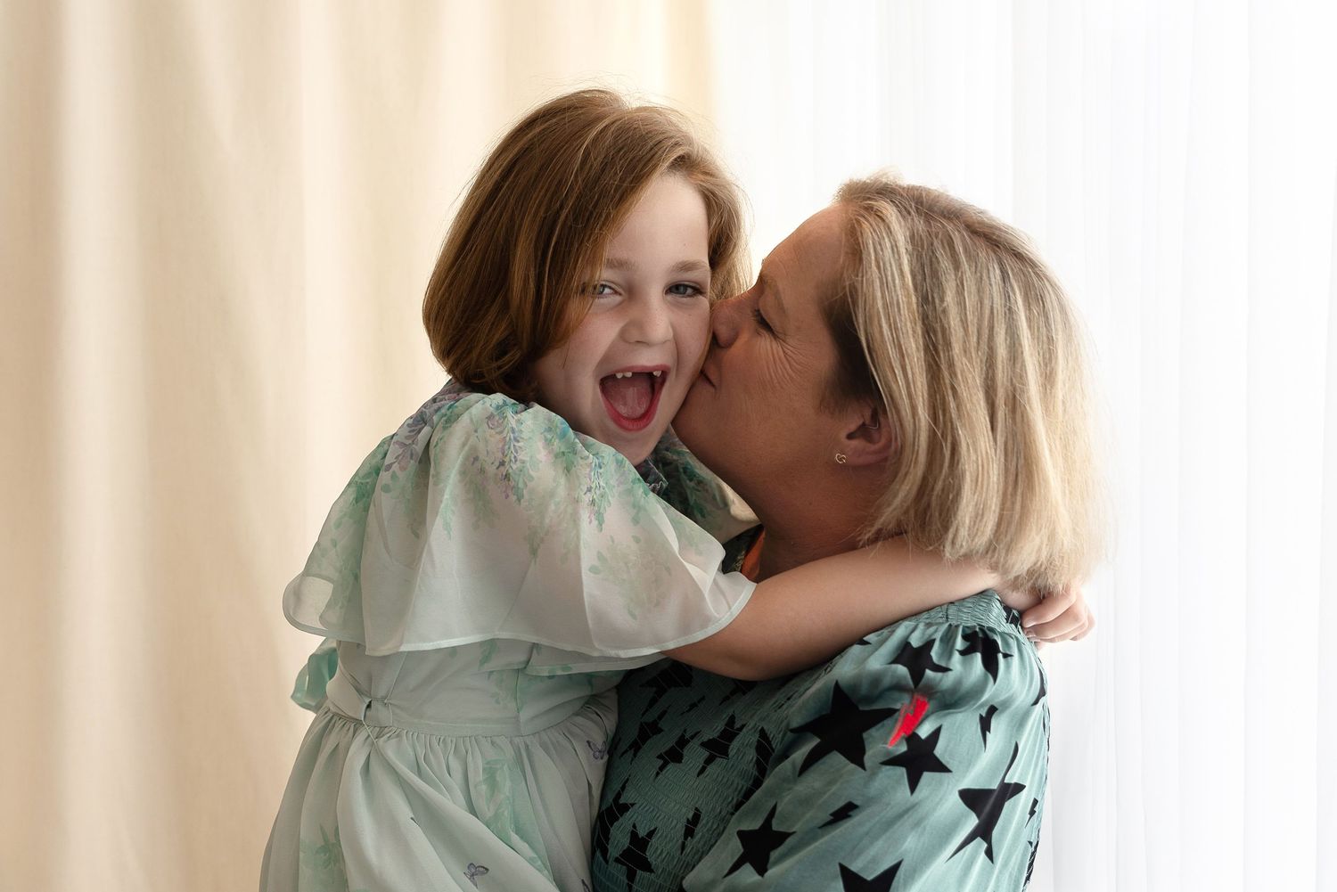 A tender moment of affection and joy between adults in mint green and patterned clothing against a light background.