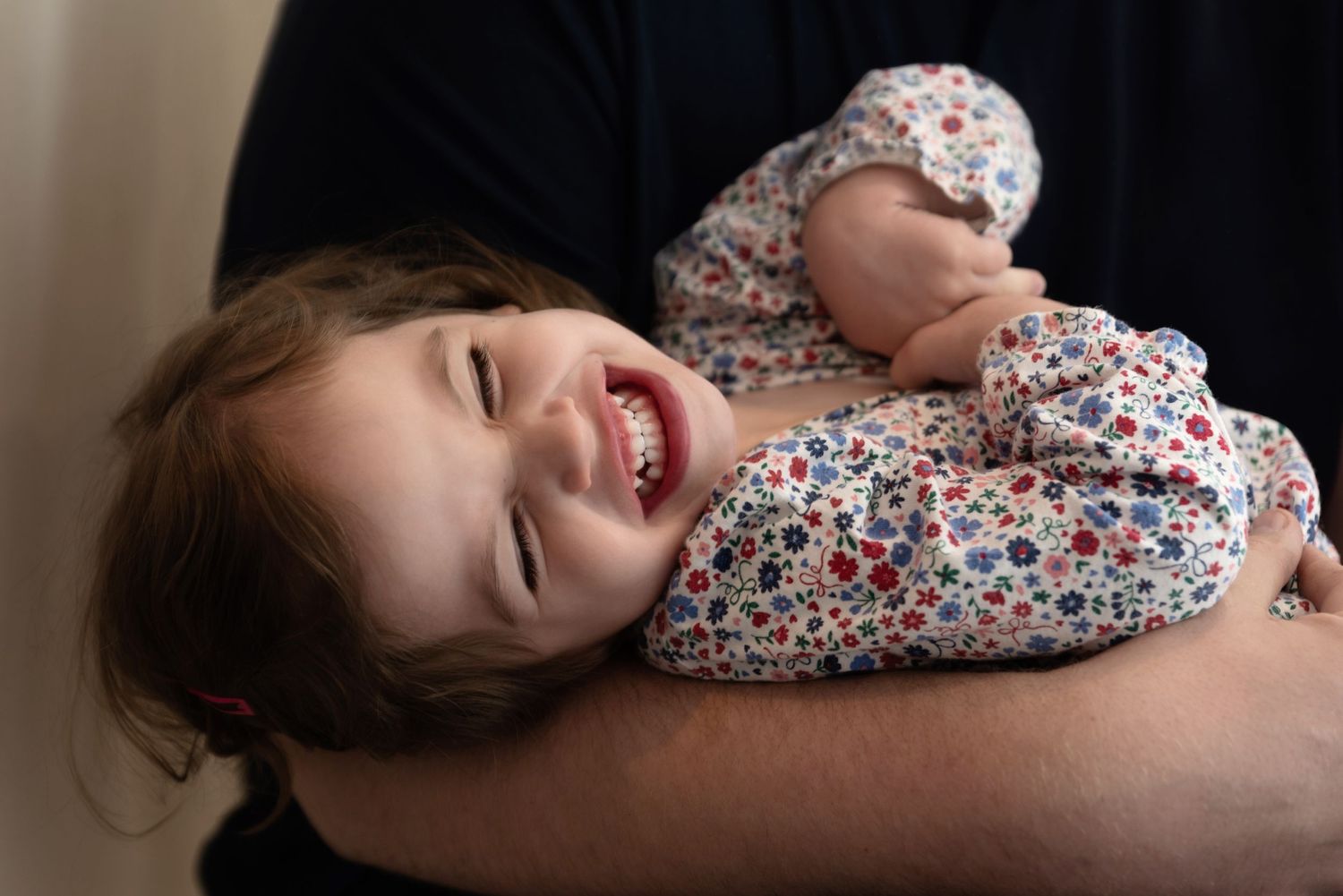 Child lying down and laughing while wearing a floral print dress.