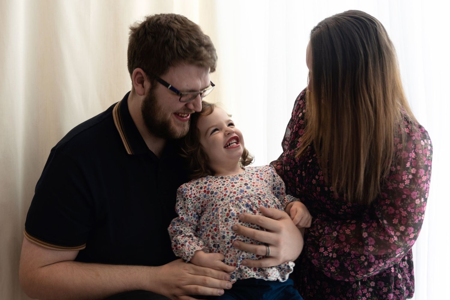 A smiling family shares a joyful moment together as they laugh and embrace on a couch.
