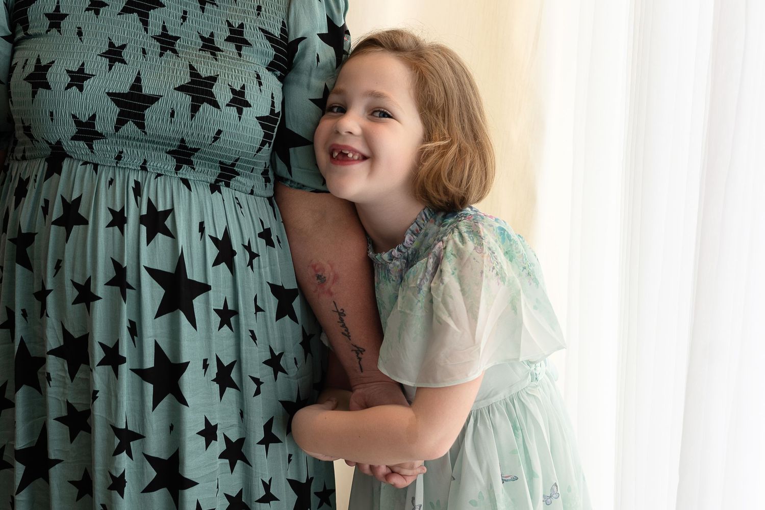 Small child in a light mint dress laughing and leaning against a teal star-patterned curtain.
