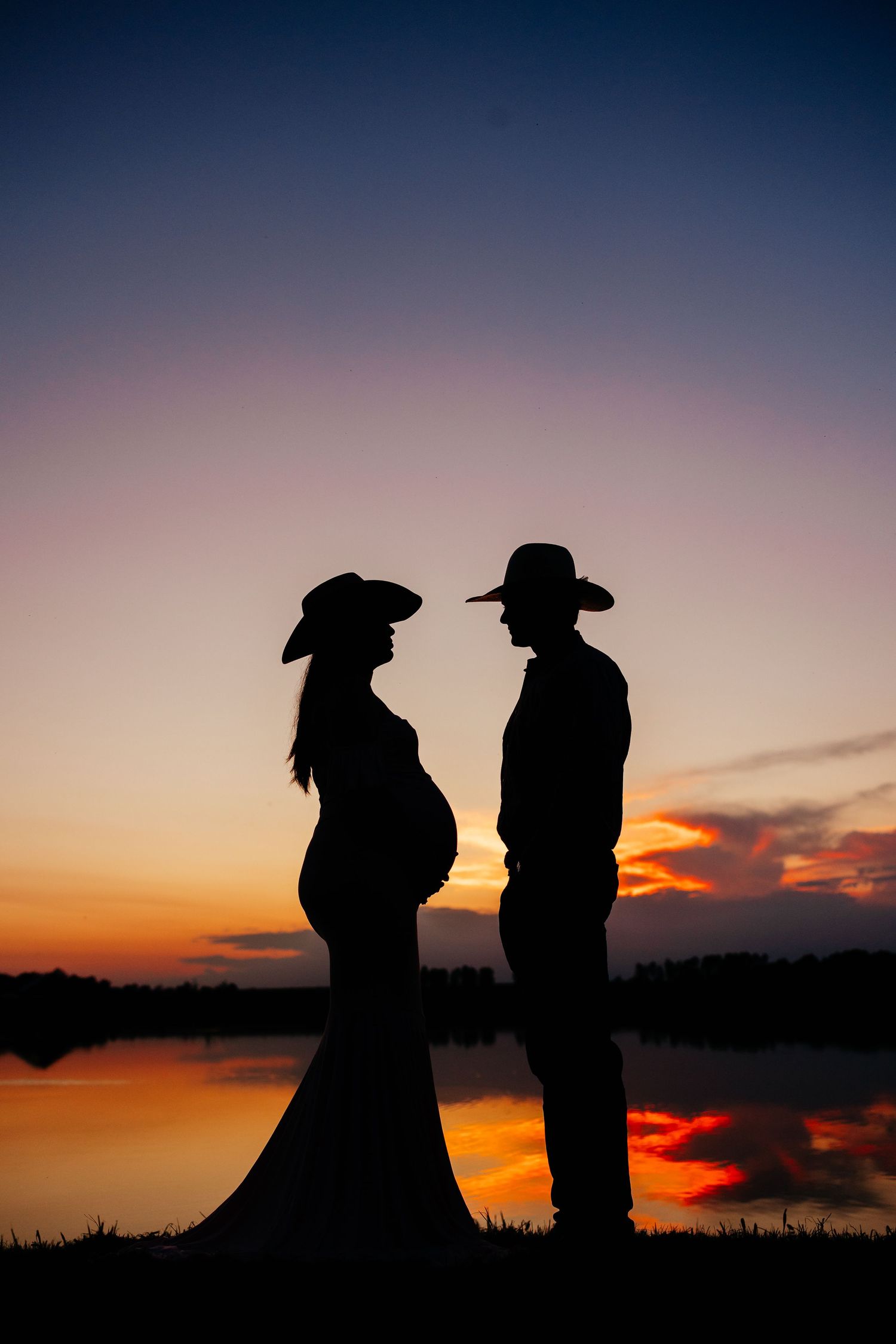 Silhouettes of two people wearing cowboy hats stand against a dramatic orange and purple sunset sky.