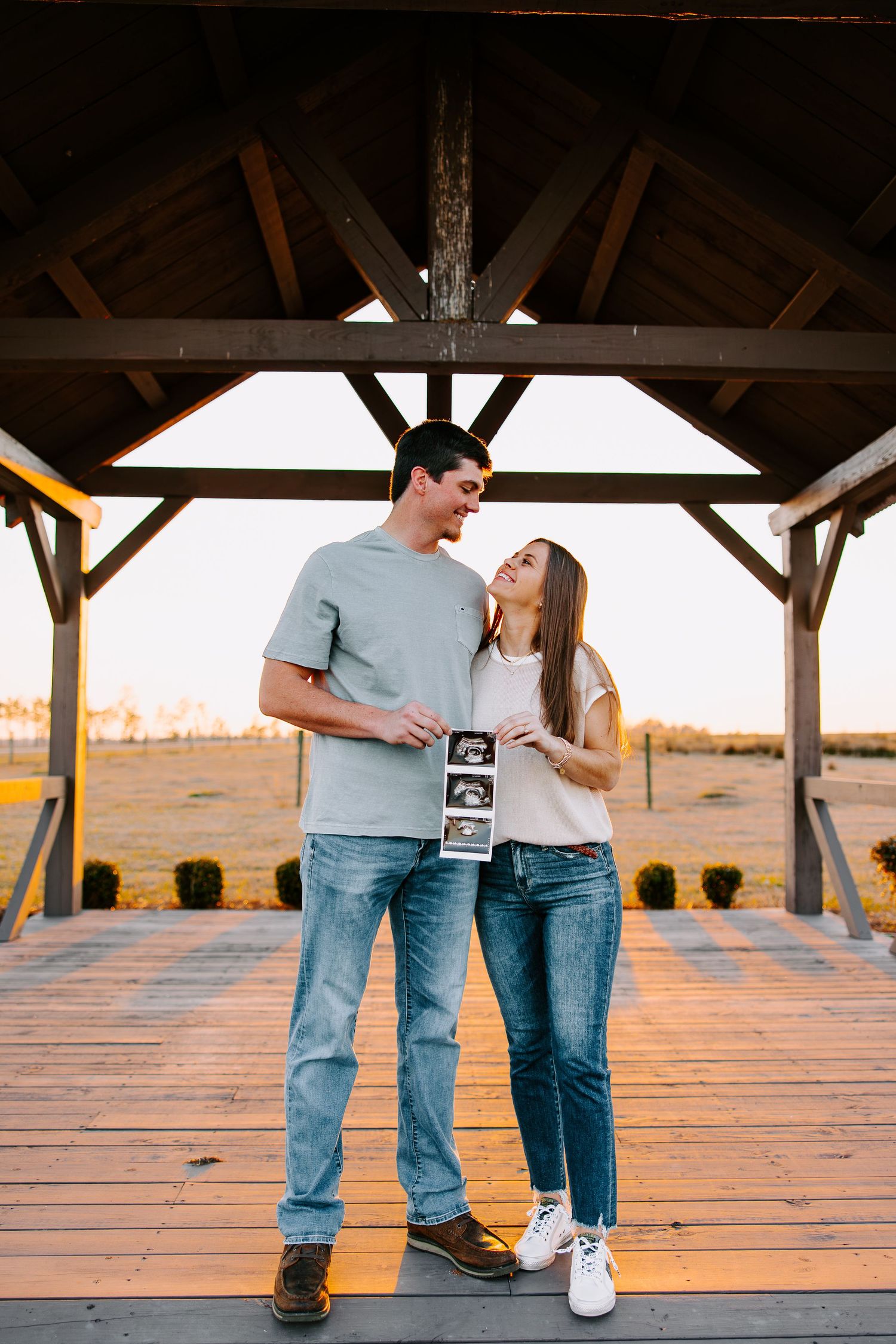 Couple sharing moment together under wooden gazebo during sunset.