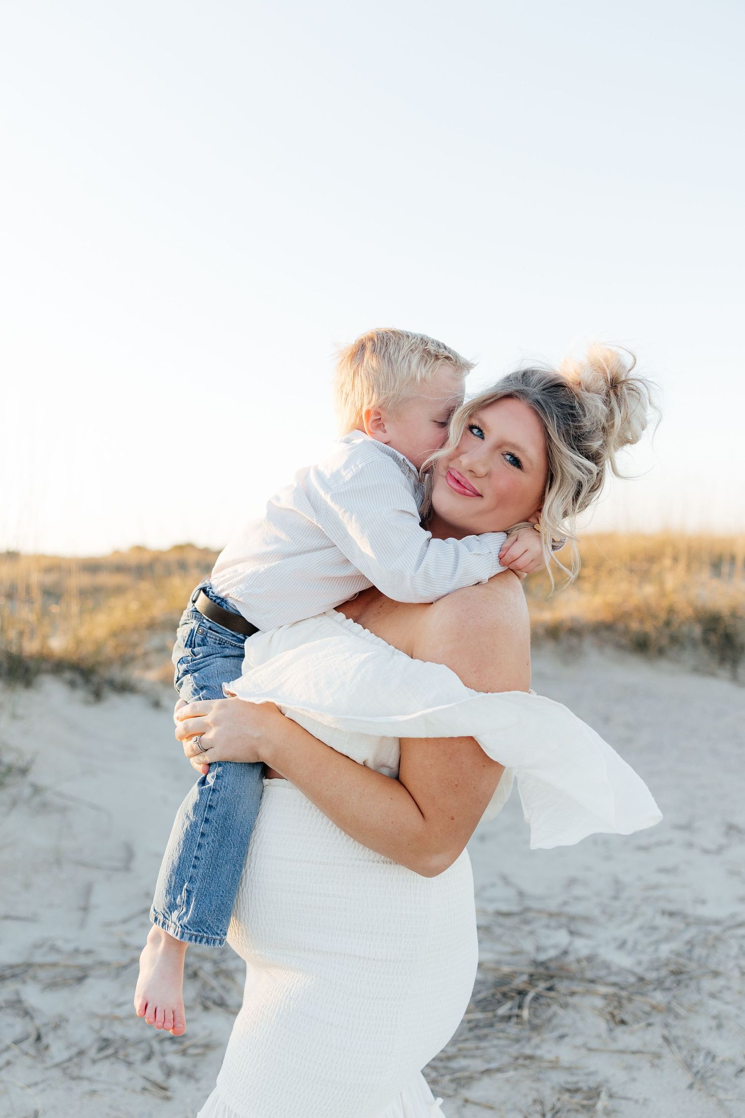 A tender moment shared between parent and child embracing on a sandy beach at sunset.