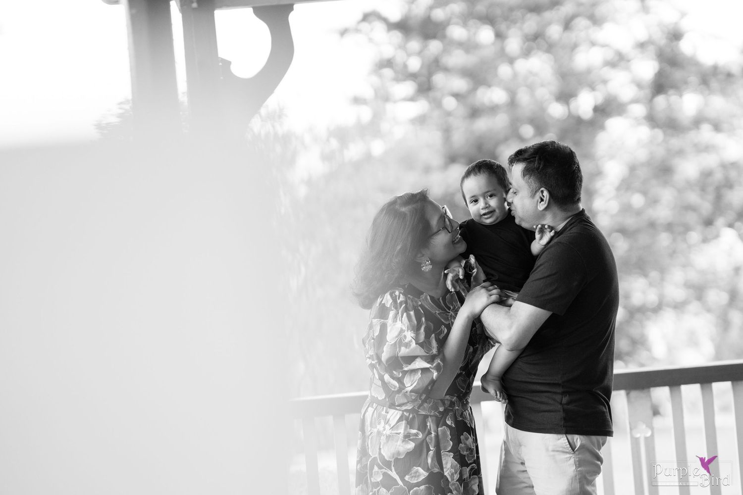 Black and white family portrait of parents holding their young child on a wooden porch - Wollongong family photographer