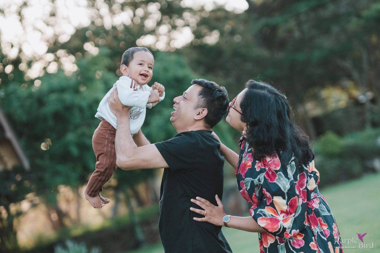 Father lifts his laughing baby into the air as the mother smiles - playful family photos with toddlers