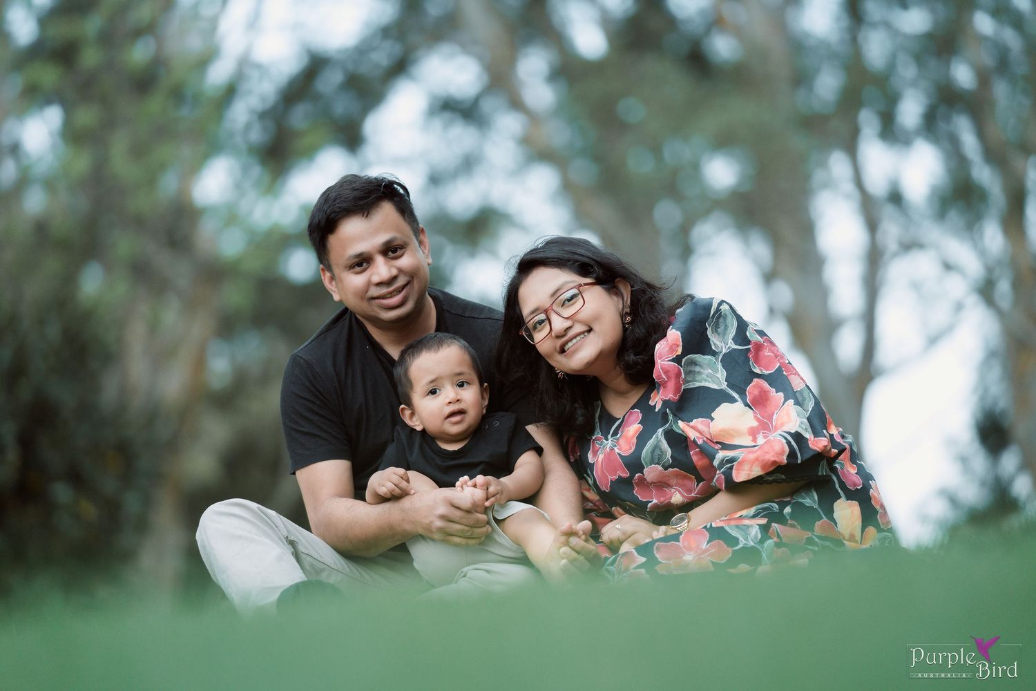Parents sit on the grass with their baby in a sunlit park - relaxed outdoor family portrait session, Wollongong