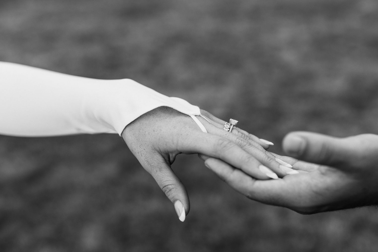 Black-and-white close-up of a couple holding hands, showing the bride’s wedding rings.