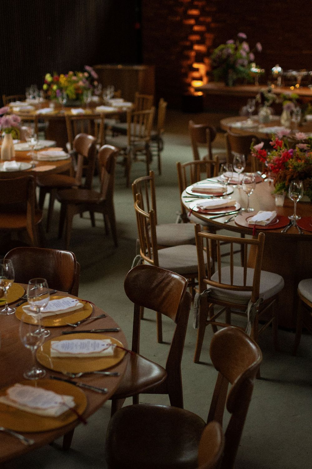 Elegant restaurant event space with round wooden tables, bentwood chairs, gold chargers, folded napkins and fresh floral centerpieces.