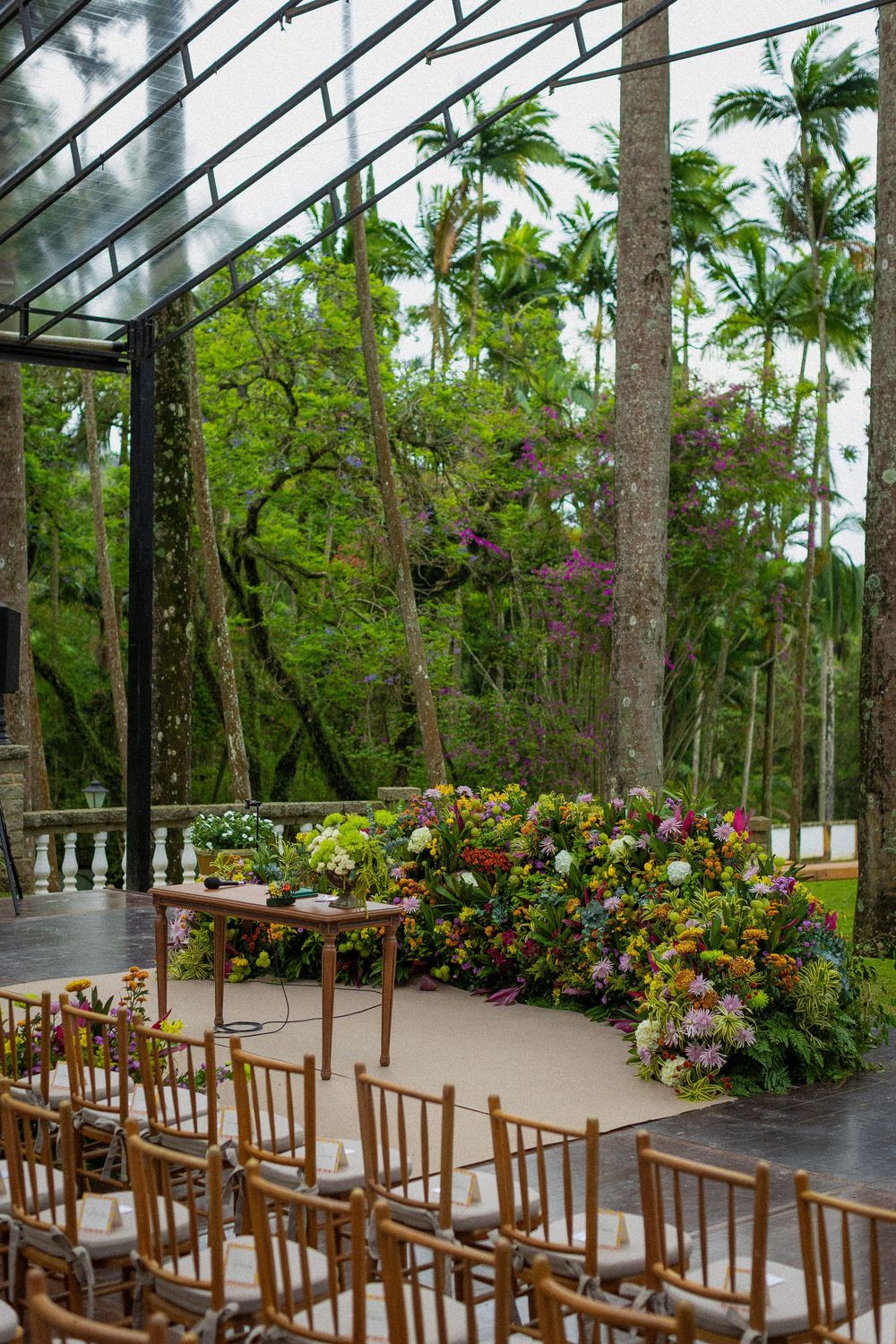 Outdoor garden wedding ceremony setup with wooden chairs, a rustic table and lush floral arrangements beneath tall palm trees.