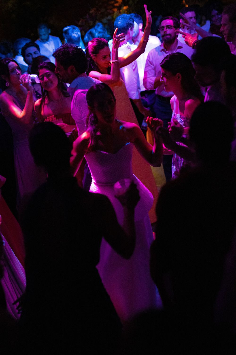Guests dance and celebrate under purple stage lighting at an evening wedding reception, with a bride in a white gown at the center.