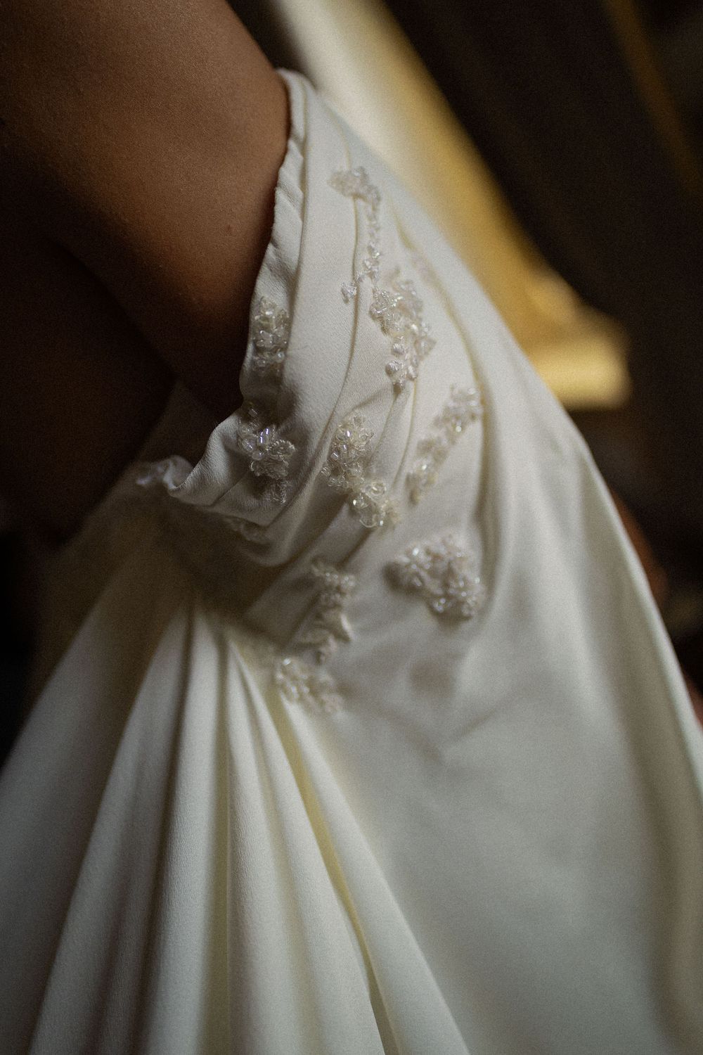 Close-up of an ivory wedding dress with gathered satin fabric and delicate beaded floral embellishments at the side.