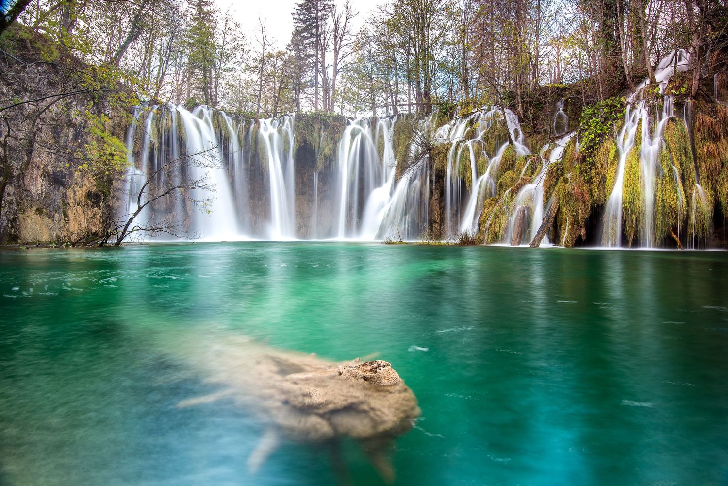Ampia cascata che scende su roccia muschiosa in un lago verde smeraldo