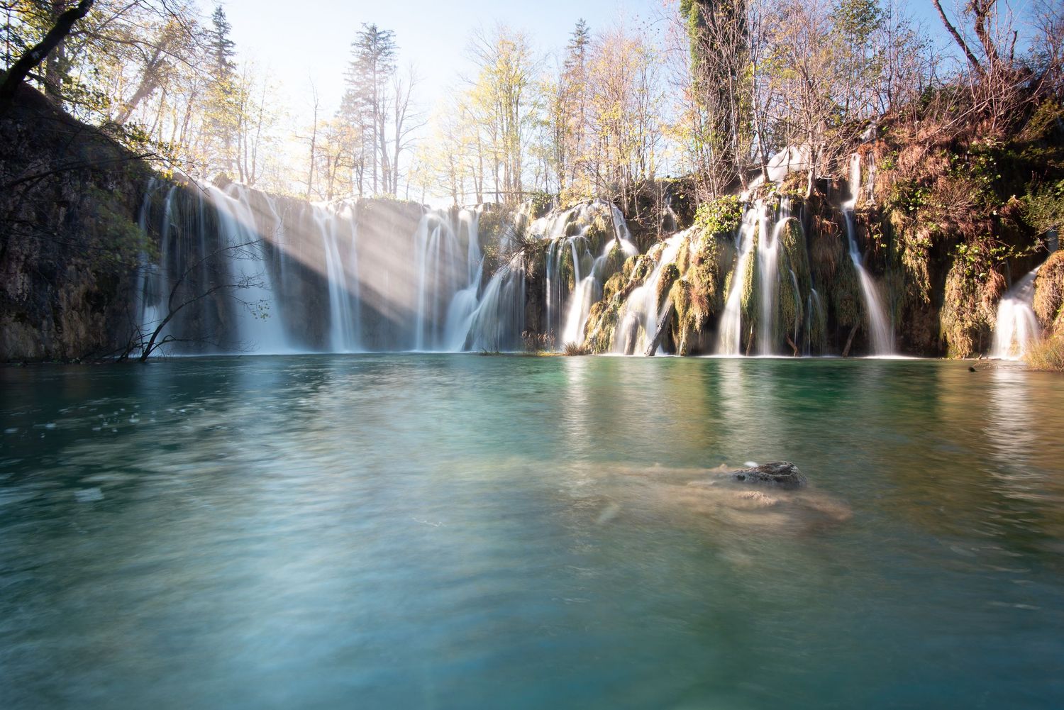 Cascata al mattino con lago turchese e roccia in primo piano