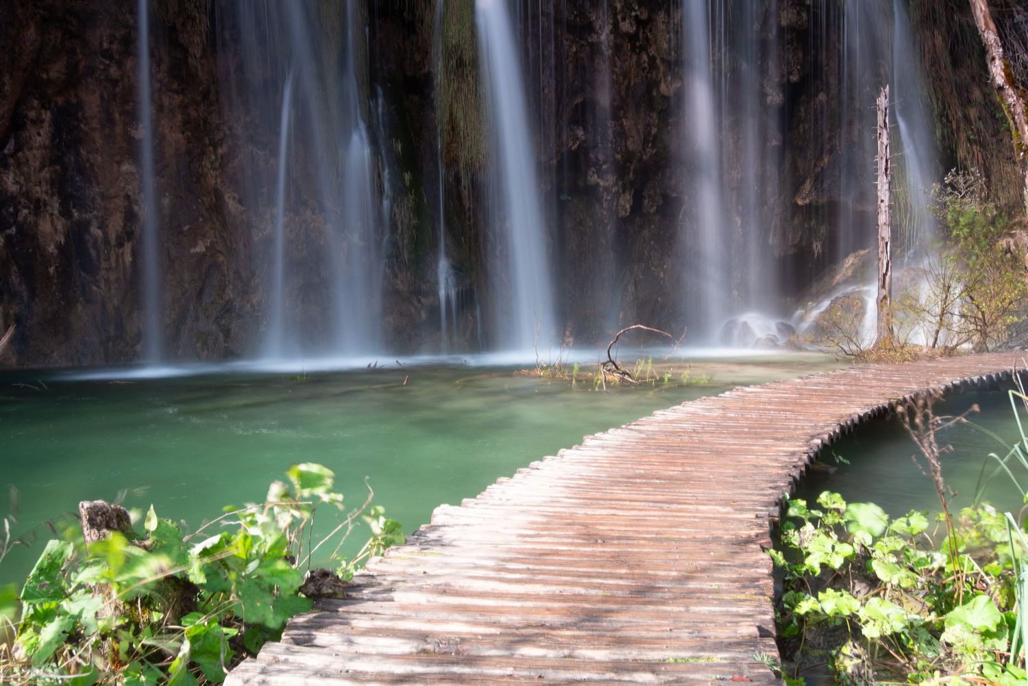 Passerella in legno davanti a una cascata sospesa sul lago
