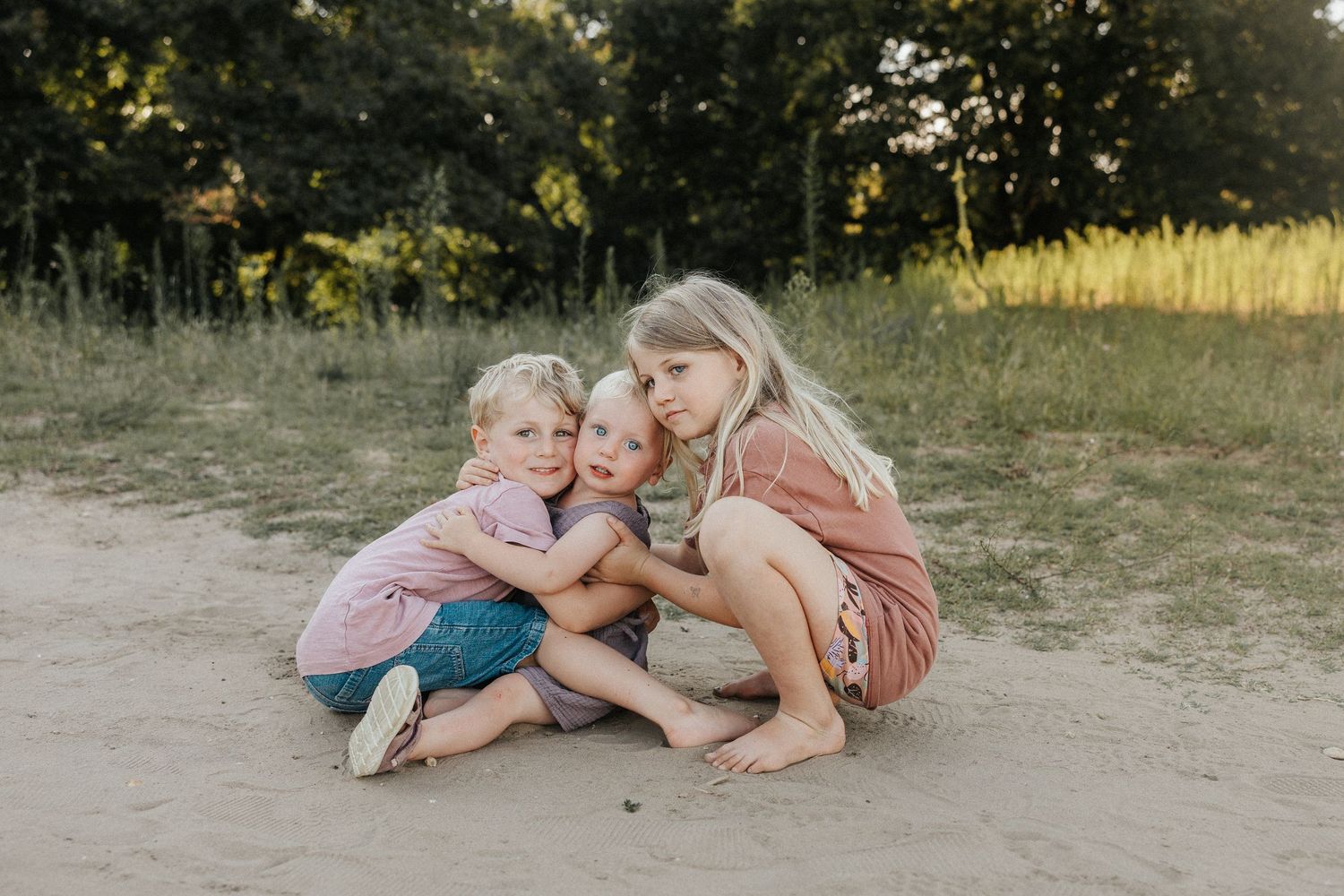 A smiling mother in a pink coat holds her toddler outdoors, sharing a tender nose-to-nose moment.