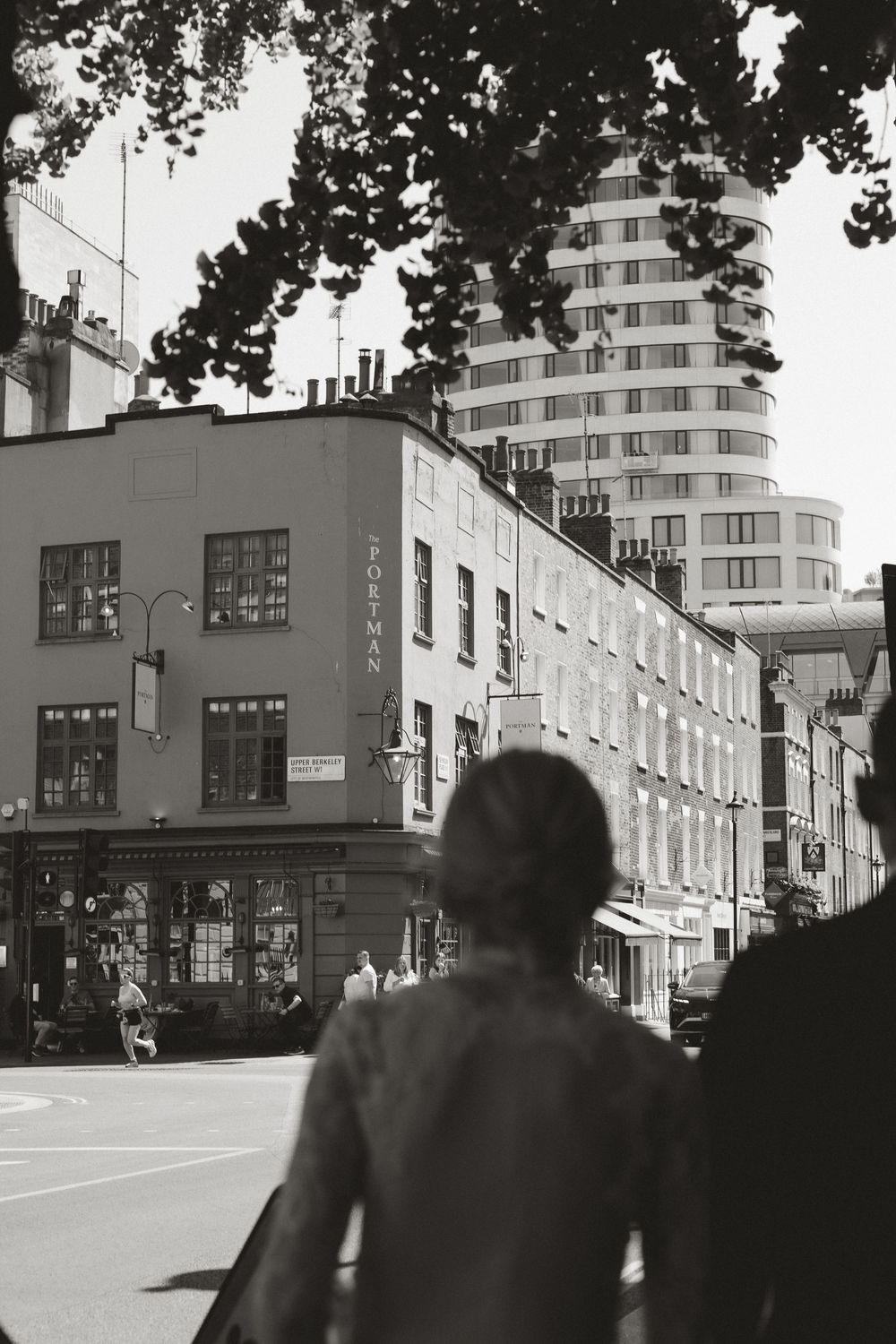 Black and white street scene with a person walking past historic buildings and a modern tower in an urban city setting.