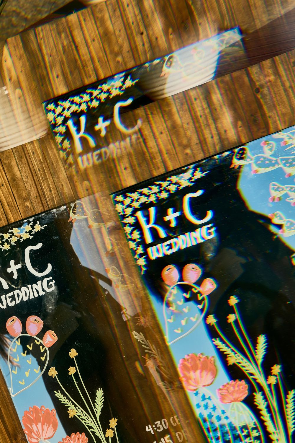 K+C wedding program cards with colorful floral designs on a wooden surface.