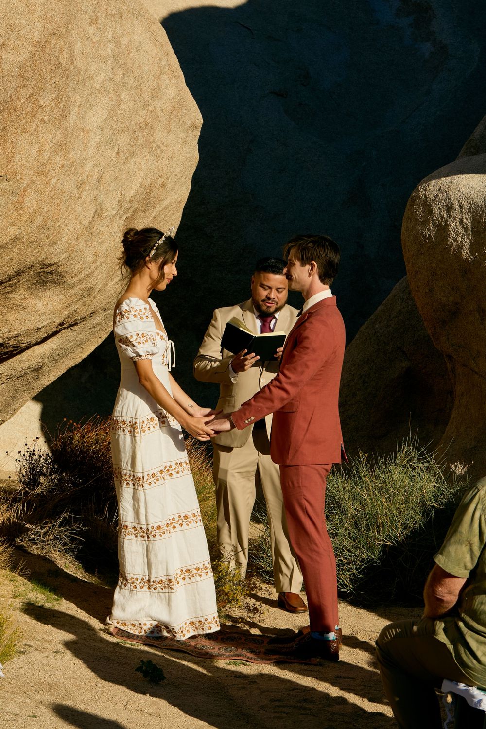 Bride and groom exchange vows outdoors among giant boulders at a rustic desert wedding ceremony.