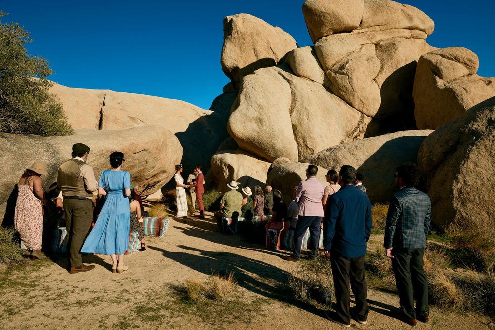 Group of people gathered among large desert boulders under a clear blue sky in an arid landscape.
