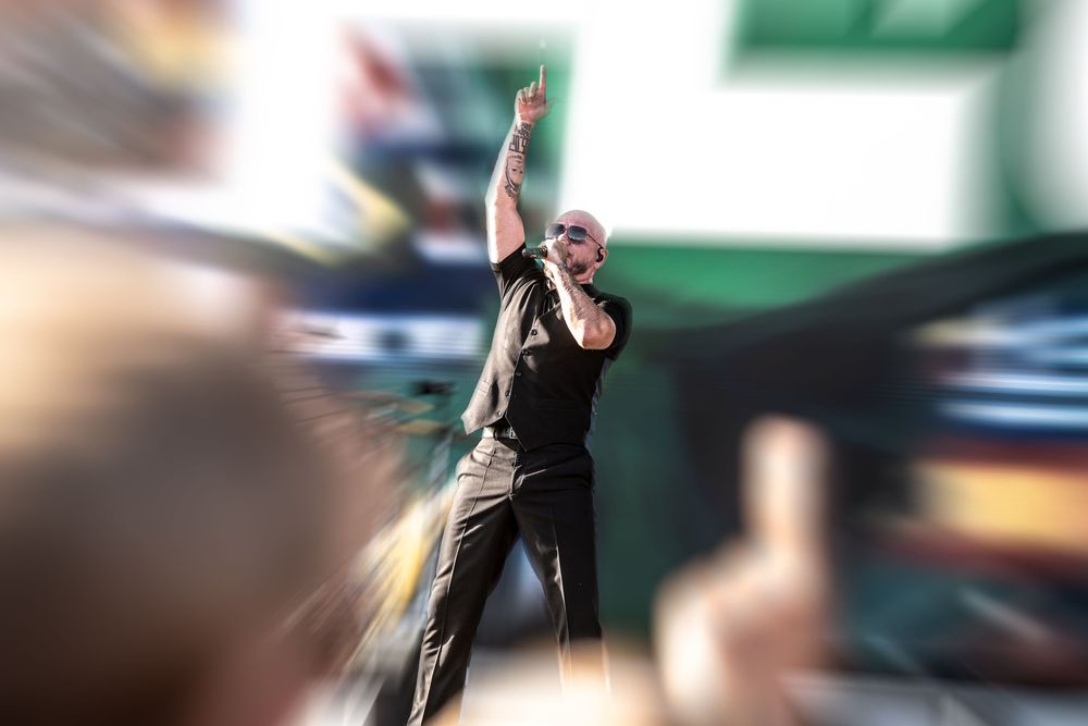 A performer in black raises one finger triumphantly on stage before an energetic crowd.