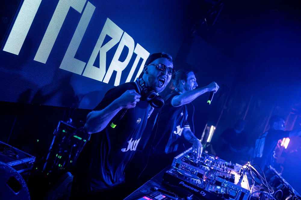 DJ performing under blue lights at a nightclub event with turntables and mixing equipment.