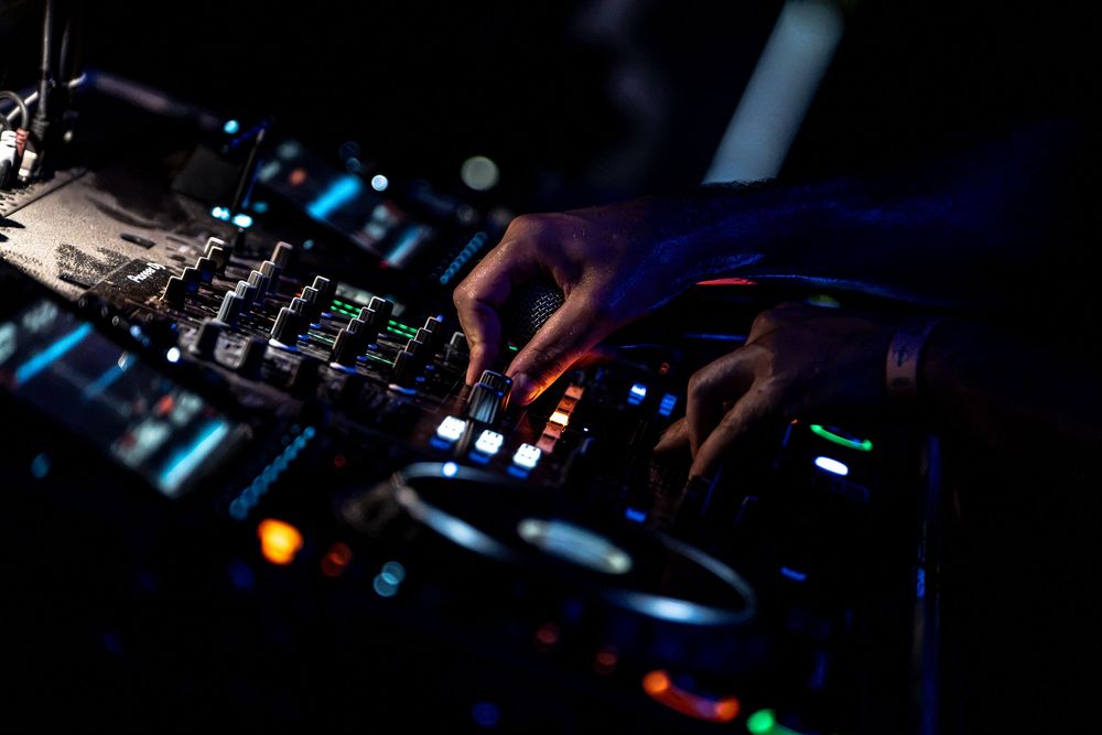DJ hands mixing music on professional turntable controller with colorful LED lights in dark nightclub.