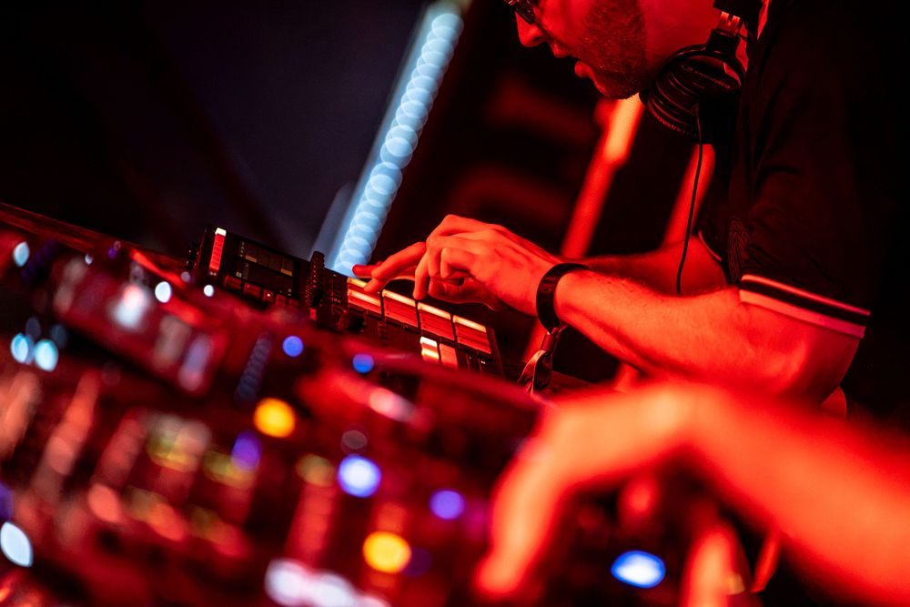 DJ performing at a nightclub under dramatic red lighting, hands on mixing equipment during a live music event.