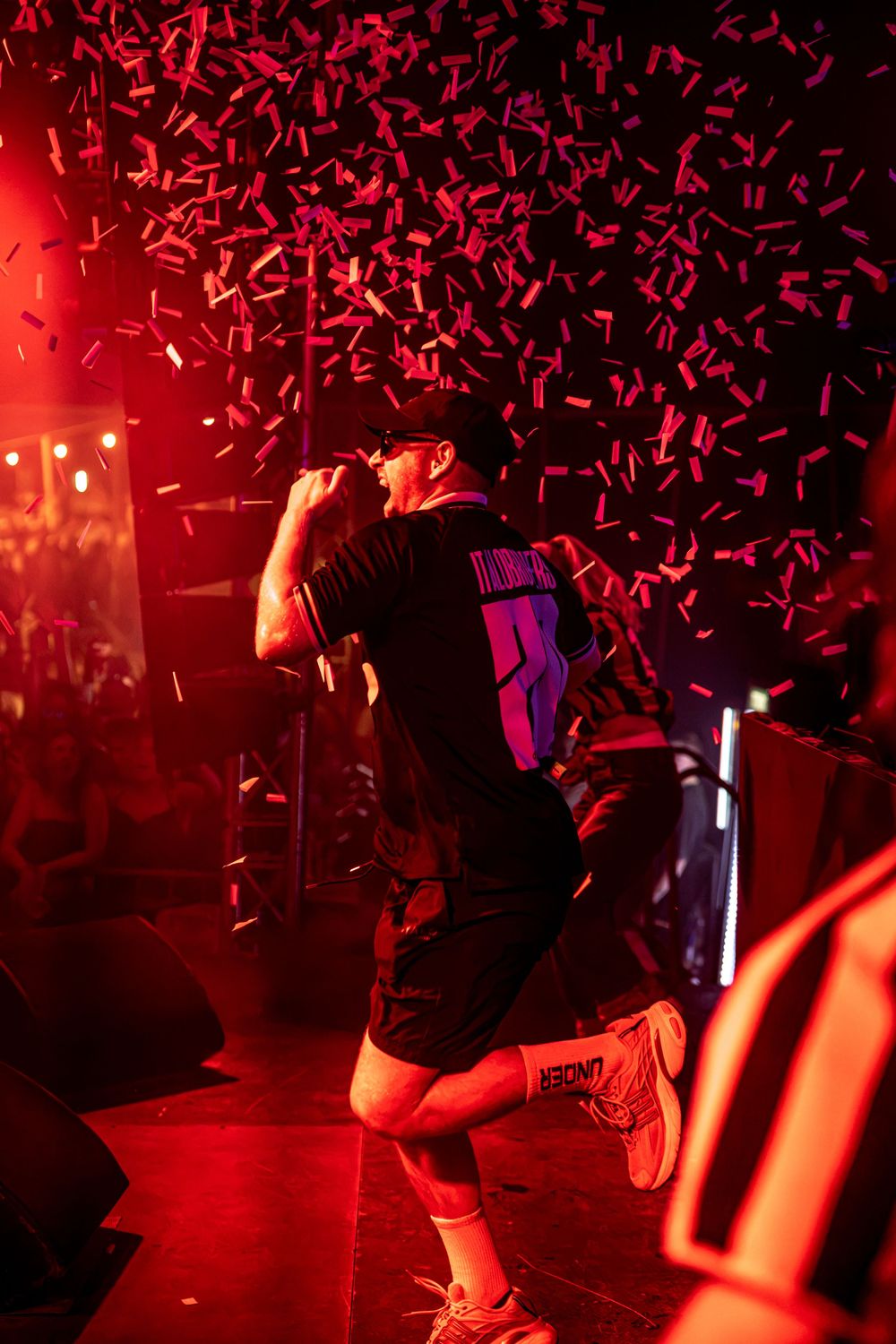 Performer on stage in red light with confetti falling during an energetic live concert.
