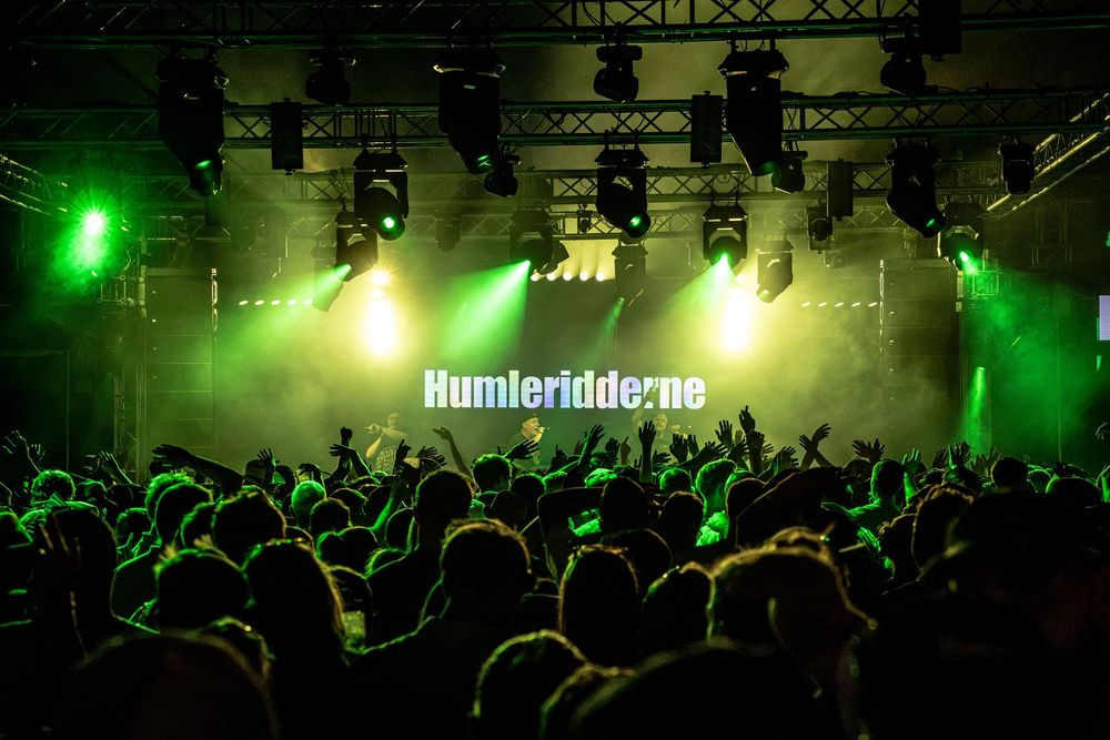 Humlerridderne performing live on stage with green lights and a large crowd at a concert.