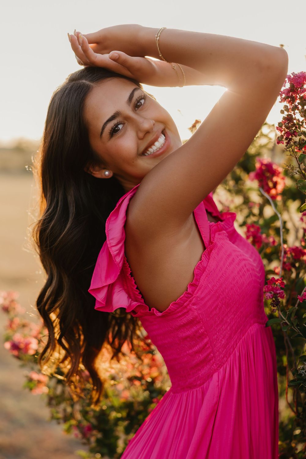 A senior girl has a dramatic pose during golden hour in Tulia, Texas in front of pink flowers wearing a matching pink dress.