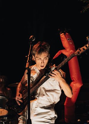 Guitarist performing on stage with a red inflatable tube man dancing in the background at a live concert.