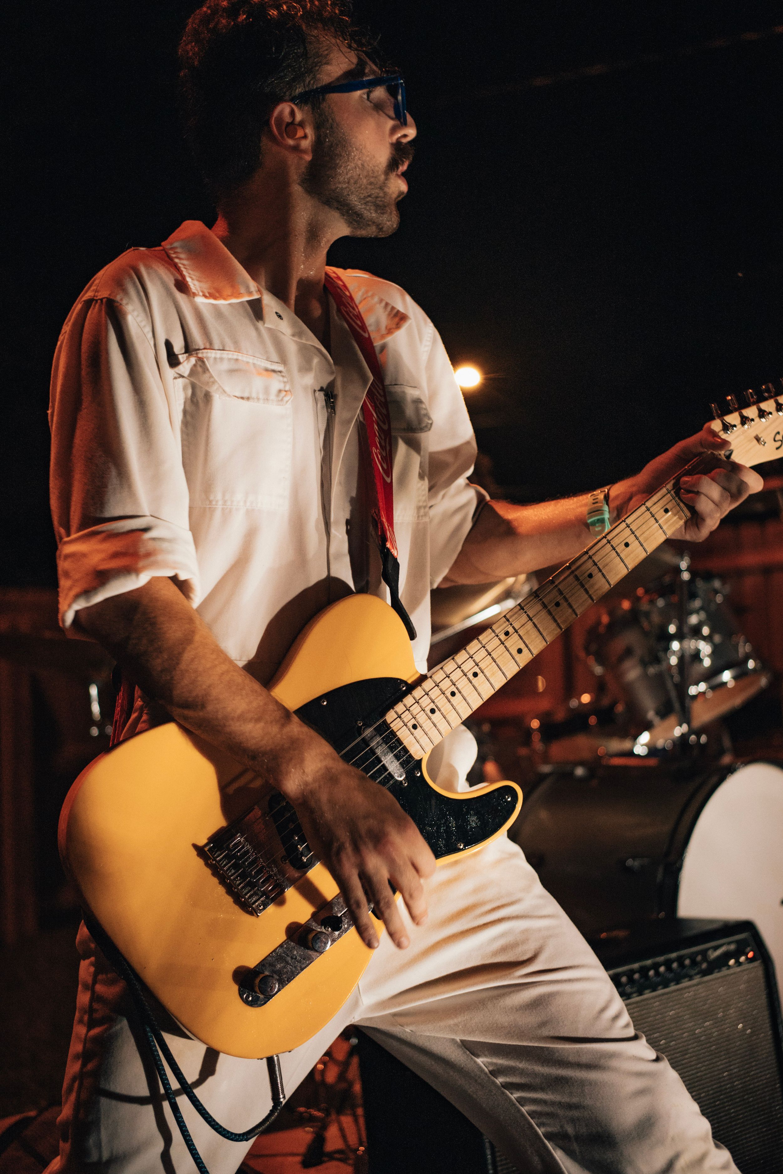 A male guitarist passionately plays a yellow Telecaster electric guitar on stage under warm lights.