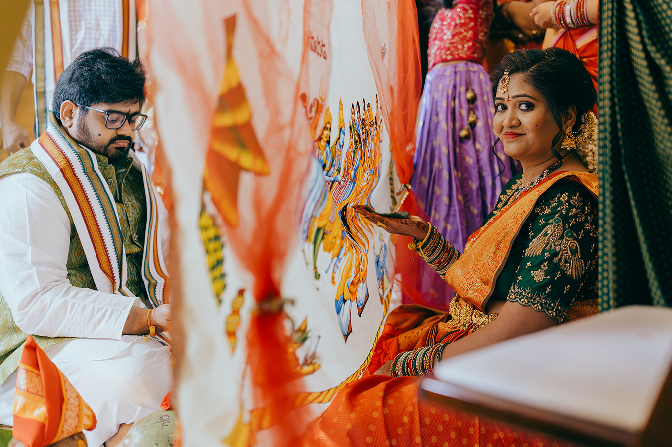 Indian couple in traditional wedding attire during Hindu ceremony, bride in green saree, groom in white kurta with orange dupatta.