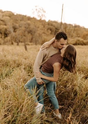 Couple sharing a romantic kiss in a golden field, man dipping woman in an embrace outdoors.